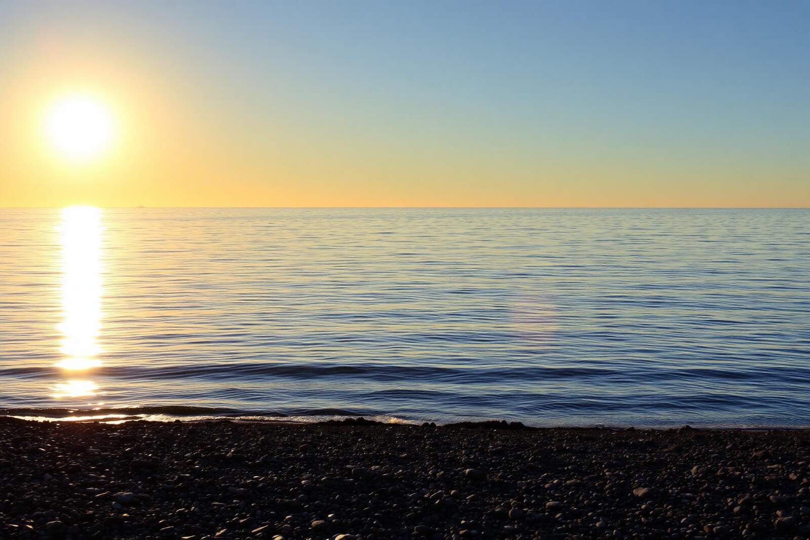 Tiefstehende Sonne spiegelt sich auf ruhigem Spätsommer-Meer über einem Kieststrand