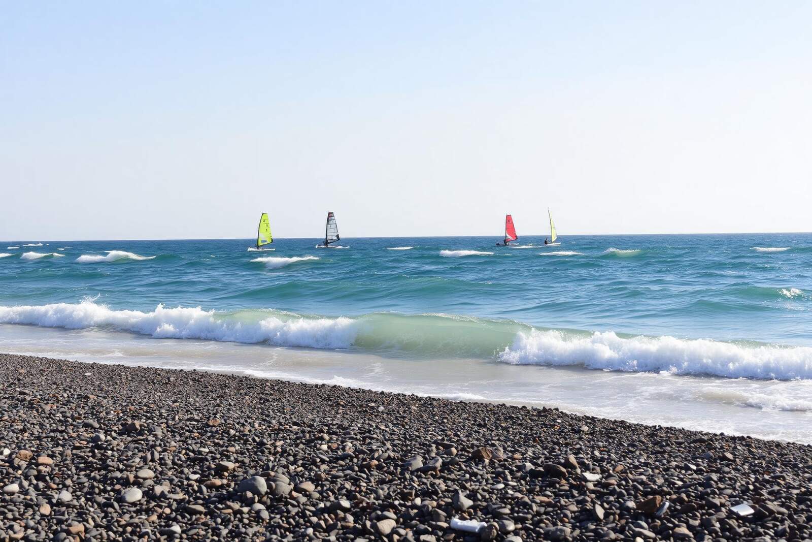 Kiesstrand mit Windsurfern in der Trianda-Bucht